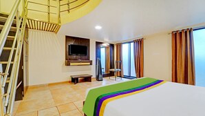 Une chambre d’hôtel avec un lit, une télévision, une chaise, un banc et un escalier.