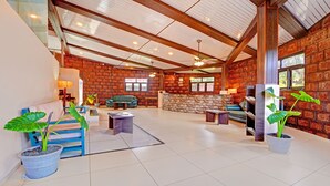 Un hall d’entrée spacieux avec un plafond haut, des poutres apparentes et un mur en briques. On y trouve plusieurs coins salon avec des canapés, ainsi qu’un comptoir d’accueil.
