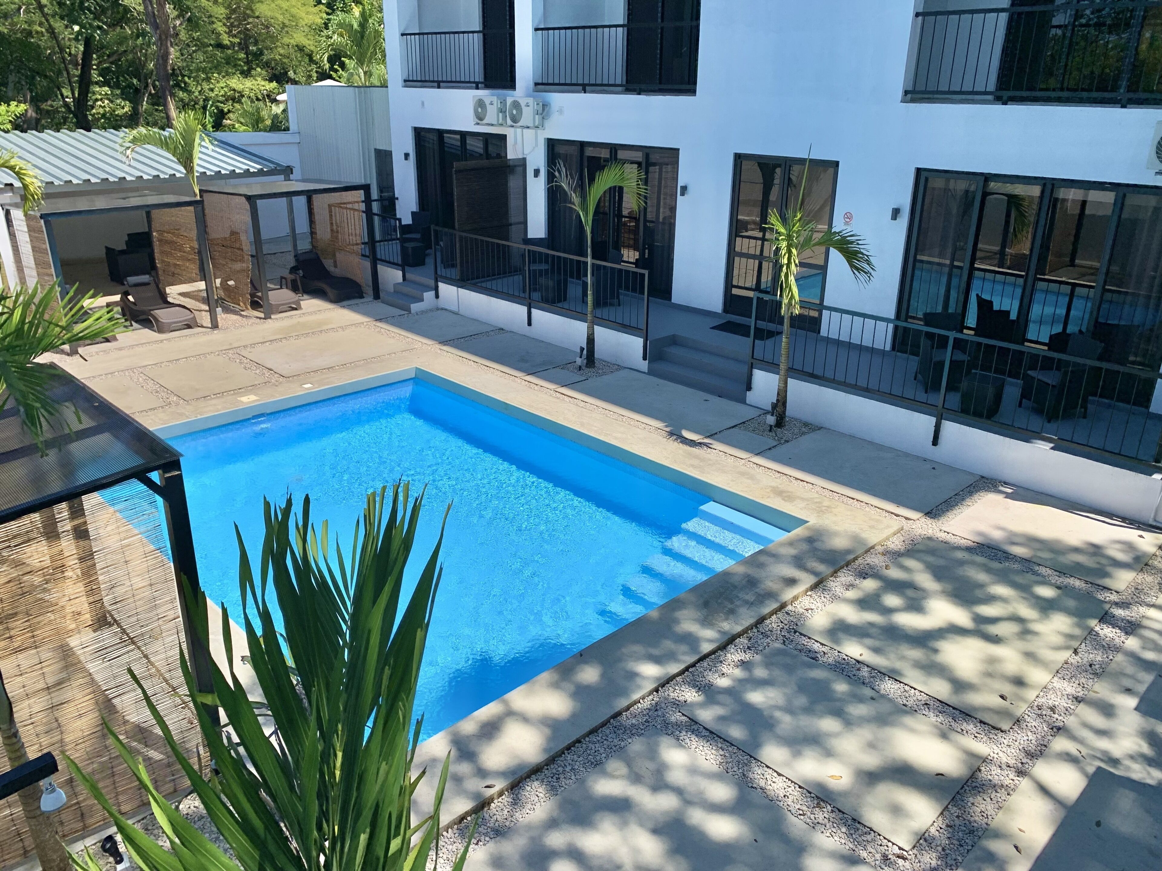 A modern building with a swimming pool, outdoor seating, and a covered patio area.