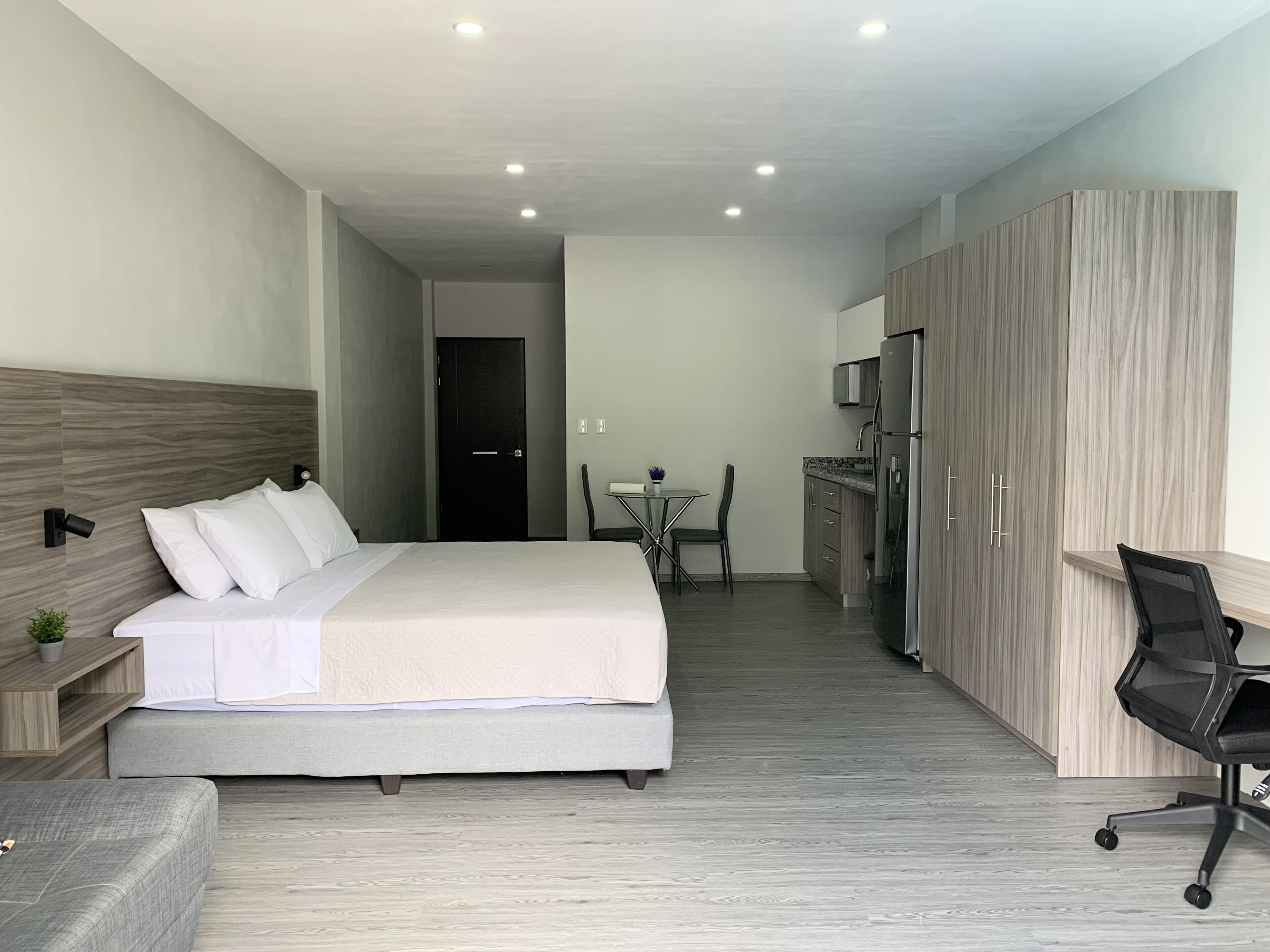 Camera d'albergo moderna con un letto, una scrivania, una sedia, un tavolino e angolo cottura.