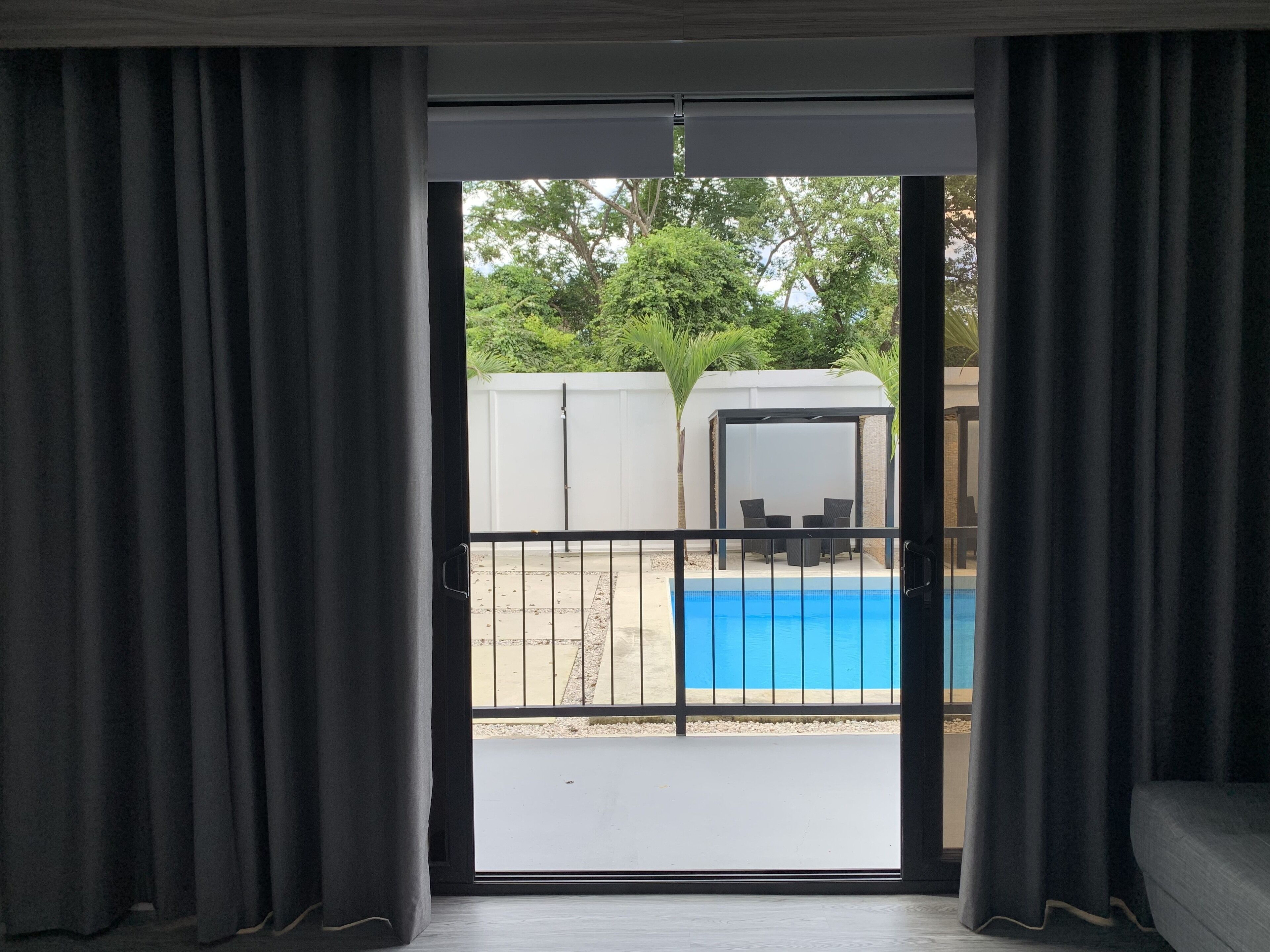 Une pièce dotée d’une porte-fenêtre coulissante donnant sur un espace extérieur comprenant une piscine et un coin salon abrité.