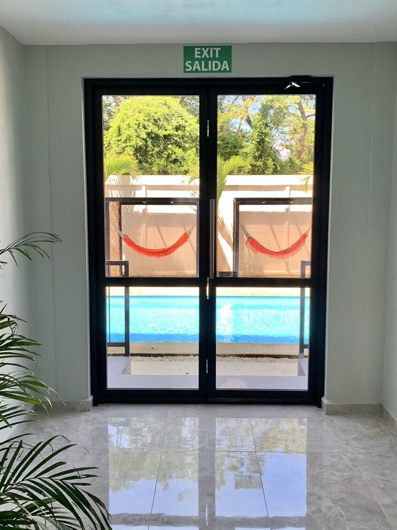 L’entrée d’un hôtel, avec un panneau indiquant la sortie, une vue sur la piscine et une plante.
