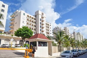 Um edifício moderno com várias varandas, um pequeno quiosque e carros estacionados na rua.