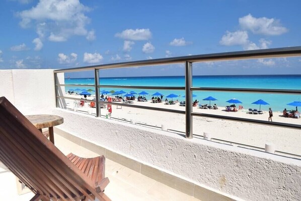 Varanda com vista para a praia, com espreguiçadeiras e guarda-sóis.