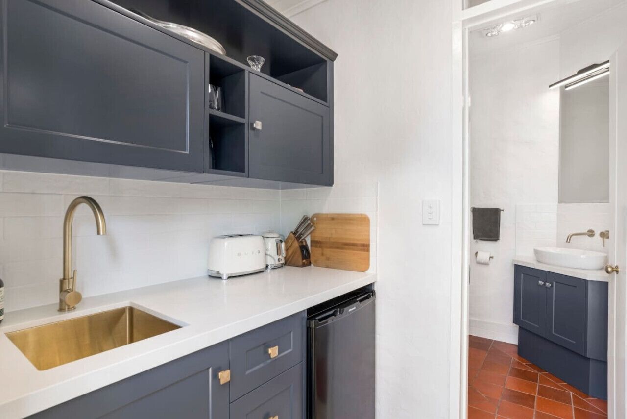 A modern kitchen with grey cabinets, a white countertop, a gold faucet, and a dishwasher.