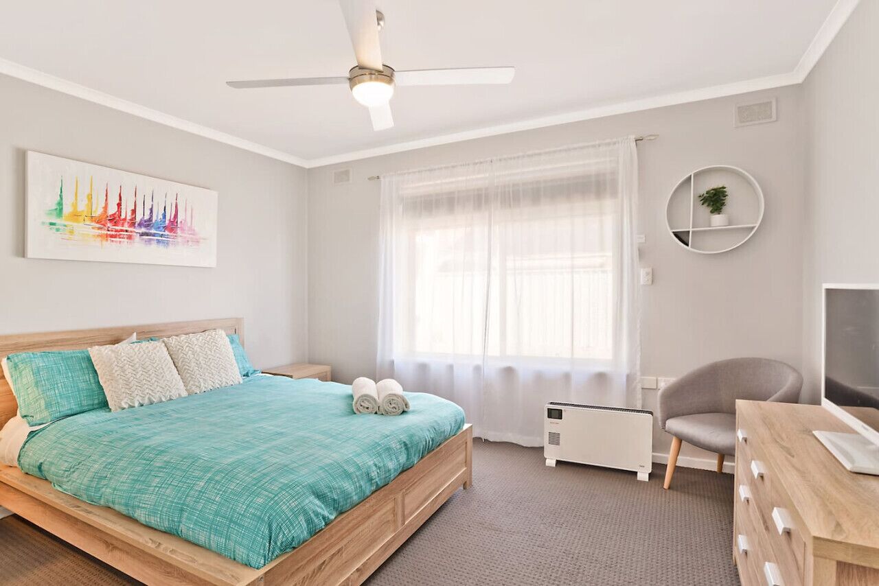 A modern bedroom with a bed, a ceiling fan, a radiator, a chair, and a desk.