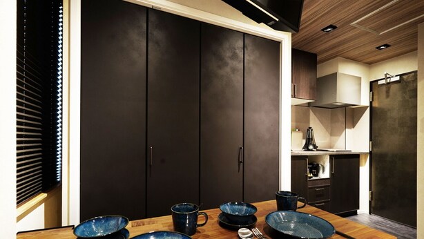 Une cuisine moderne avec des meubles de couleur sombre, une table à manger en bois agrémentée de bols bleus et une fenêtre avec des stores.