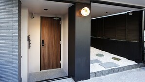 Une entrée moderne avec une porte en bois, un pilier noir et un luminaire.