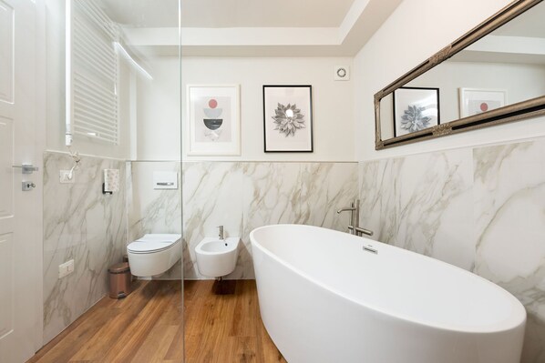 A modern bathroom with a freestanding bathtub, a bidet, and marble walls.