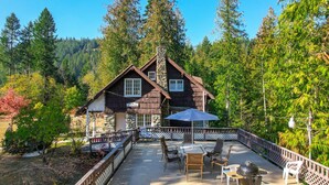 A cabin with a stone chimney, a deck with outdoor furniture, and a forested backdrop. - The Kirtland Cutter Rock House - Metaline Falls (Metaline Falls)