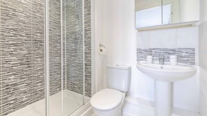 Ein Badezimmer mit Duschkabine aus Glas, Toilette und Waschbecken mit Spiegel darüber.