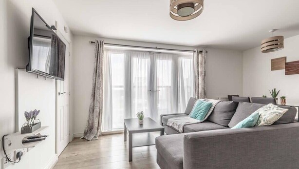 Ein modernes Wohnzimmer mit einer grauen Couch, einem Couchtisch und einem flachbildfernseher an der Wand.