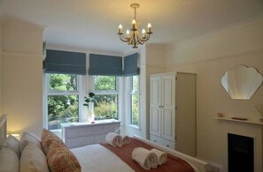A bedroom with a bed, a window with a view of greenery, a white wardrobe, and a chandelier.