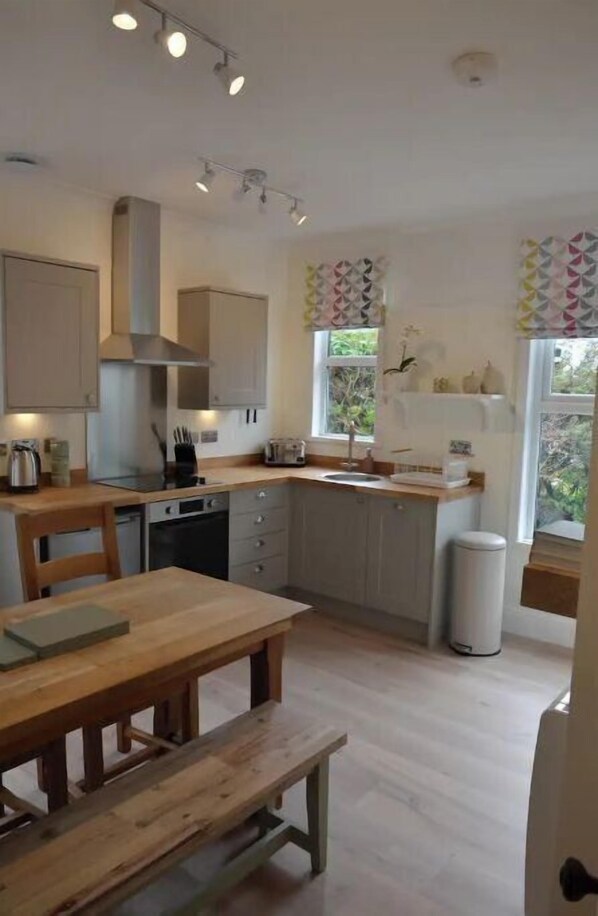 A modern kitchen with wooden cabinetry, a built-in oven, and a dining area with a wooden table and bench.
