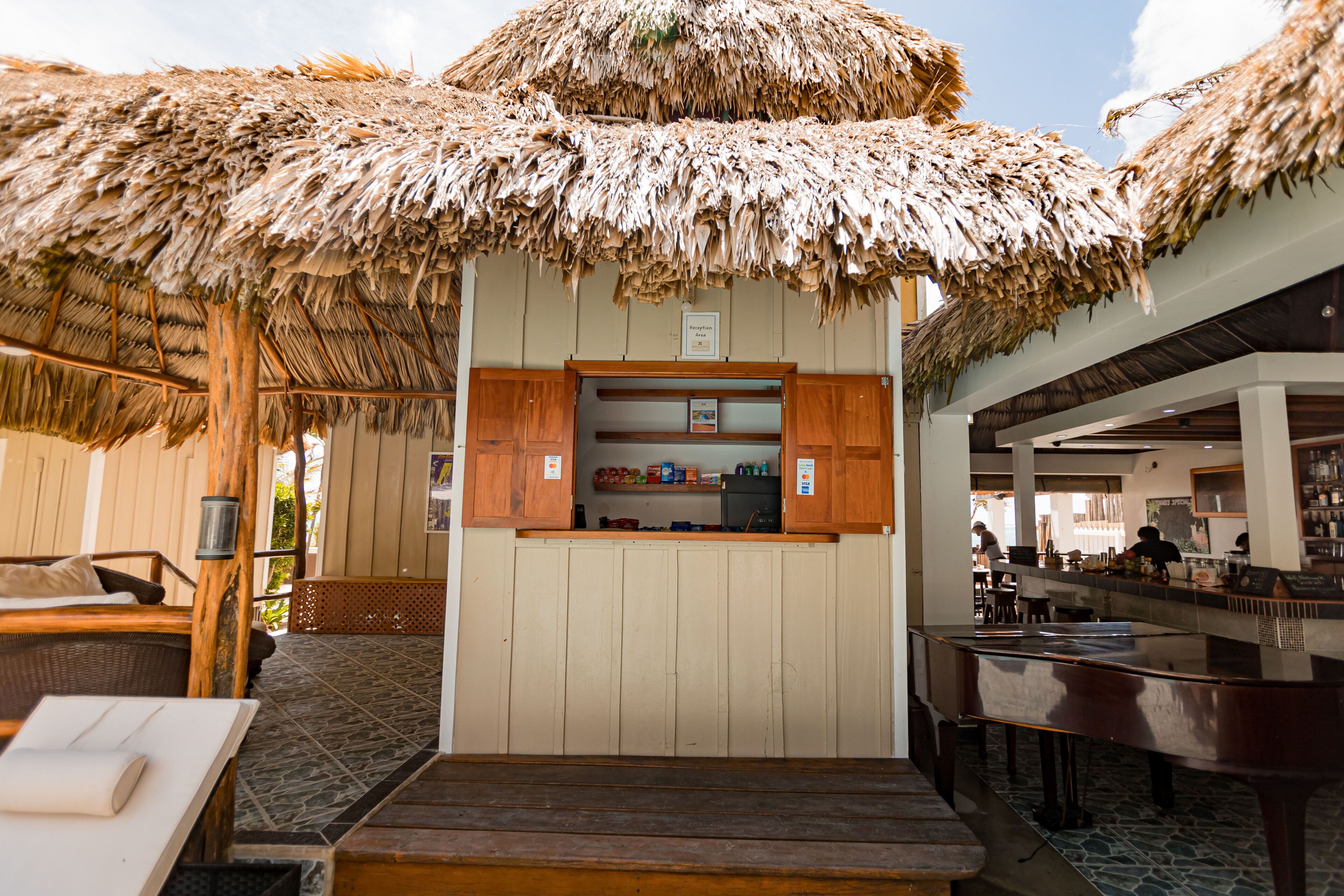 Zona bar in spiaggia con ombrelloni di paglia, un bancone e posti a sedere.