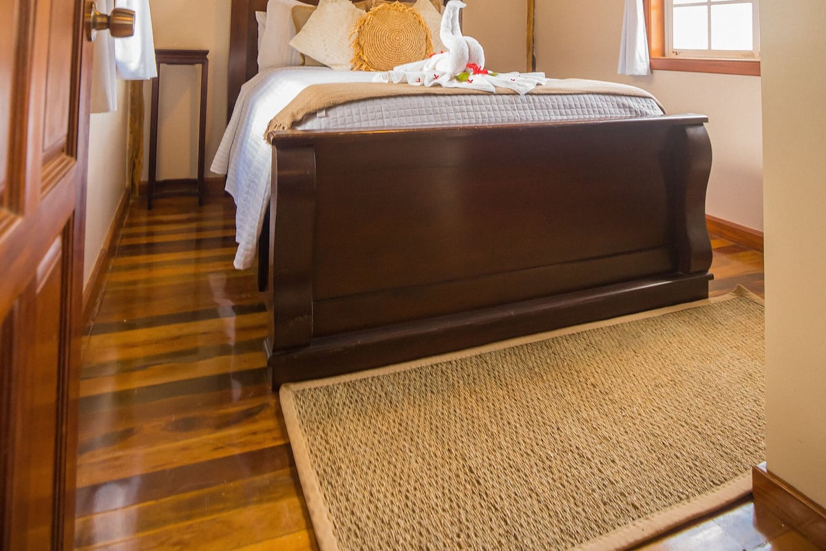 Een slaapkamer met een houten plafond, een bed met wit beddengoed, een houten vloer en een raam met gordijnen.