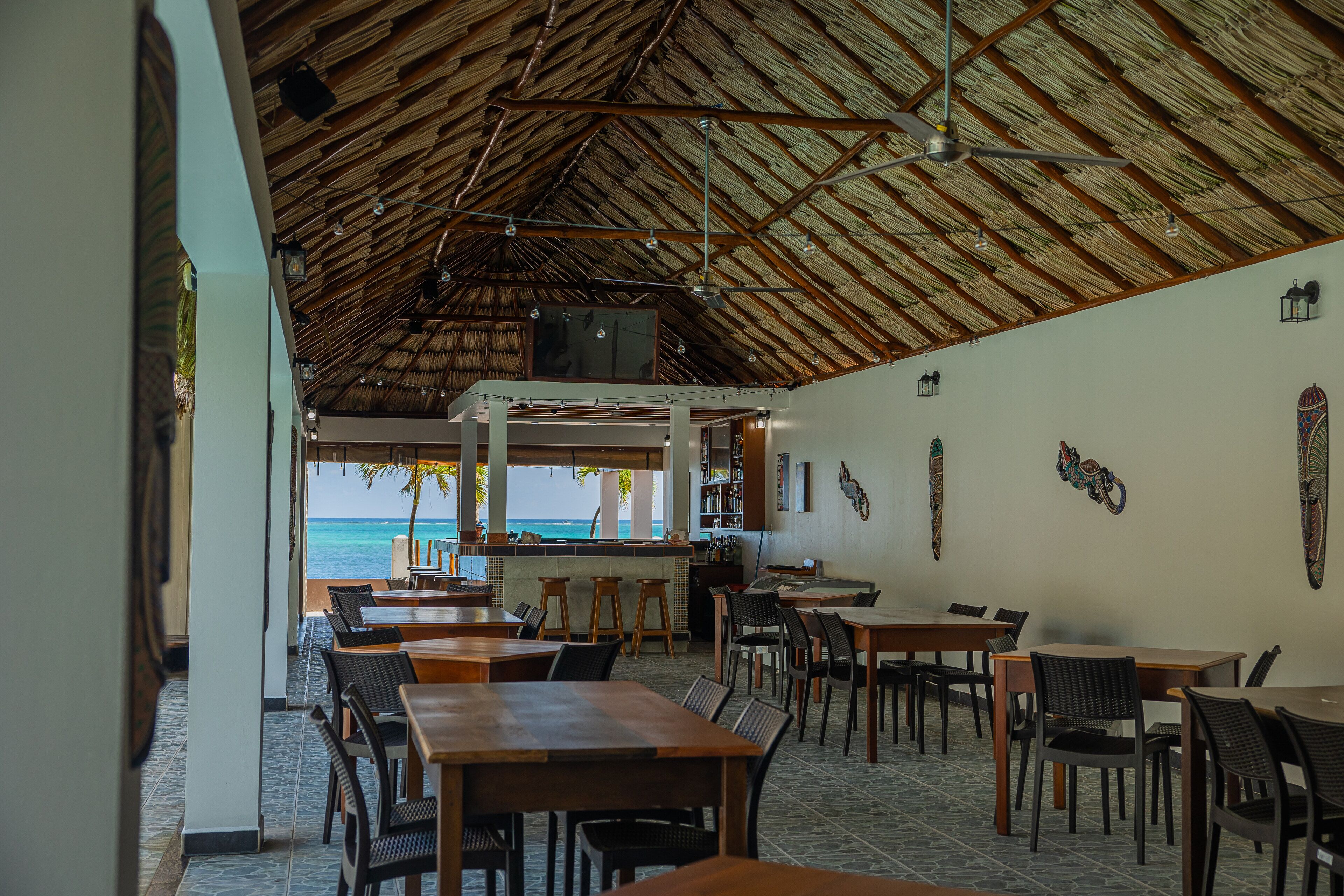 A restaurant with a thatched roof, wooden tables and chairs, and a view of the ocean.