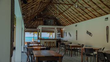 A restaurant with a thatched roof, wooden tables and chairs, and a view of the ocean.