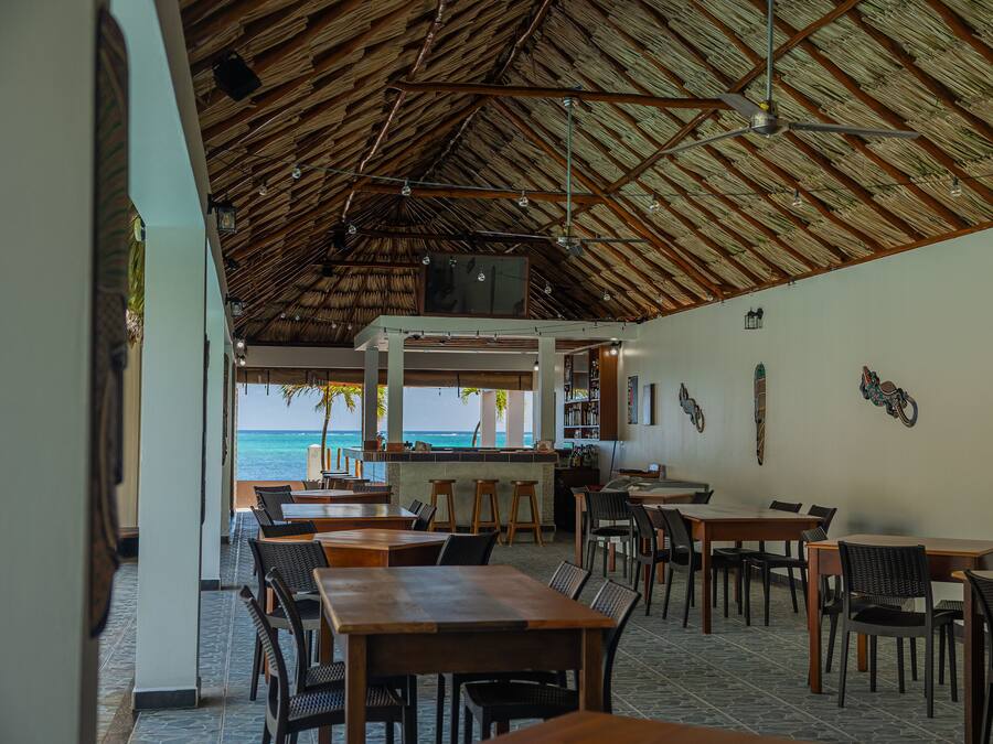 A restaurant with a thatched roof, wooden tables and chairs, and a view of the ocean.