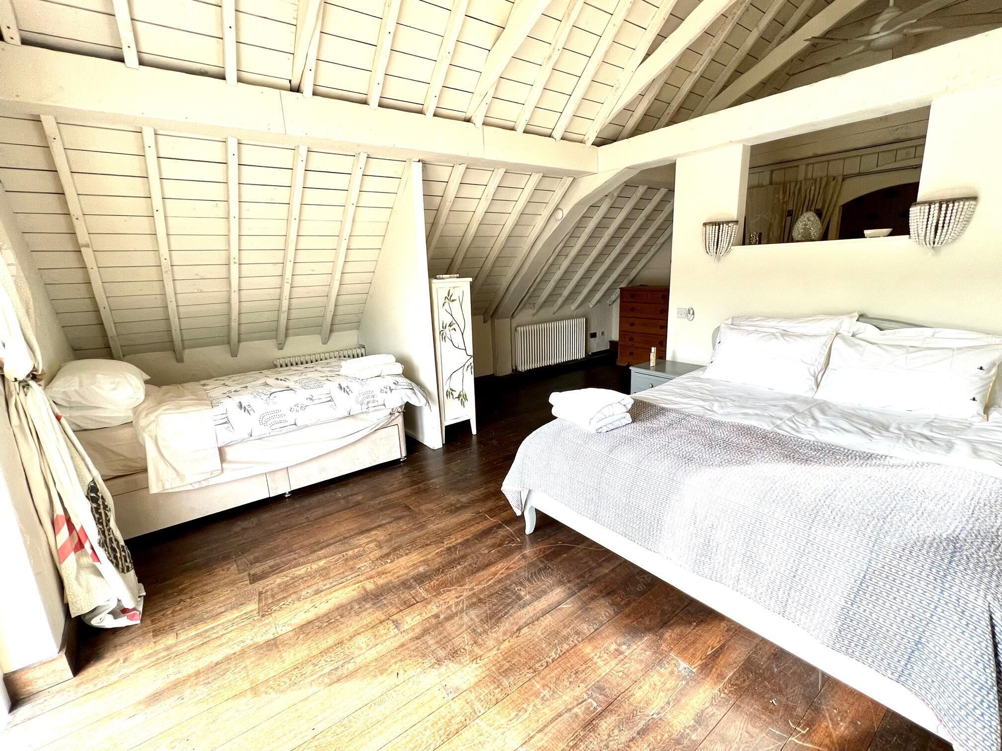 A bedroom with a sloped ceiling, wooden flooring, a bed, a dresser, and a radiator.