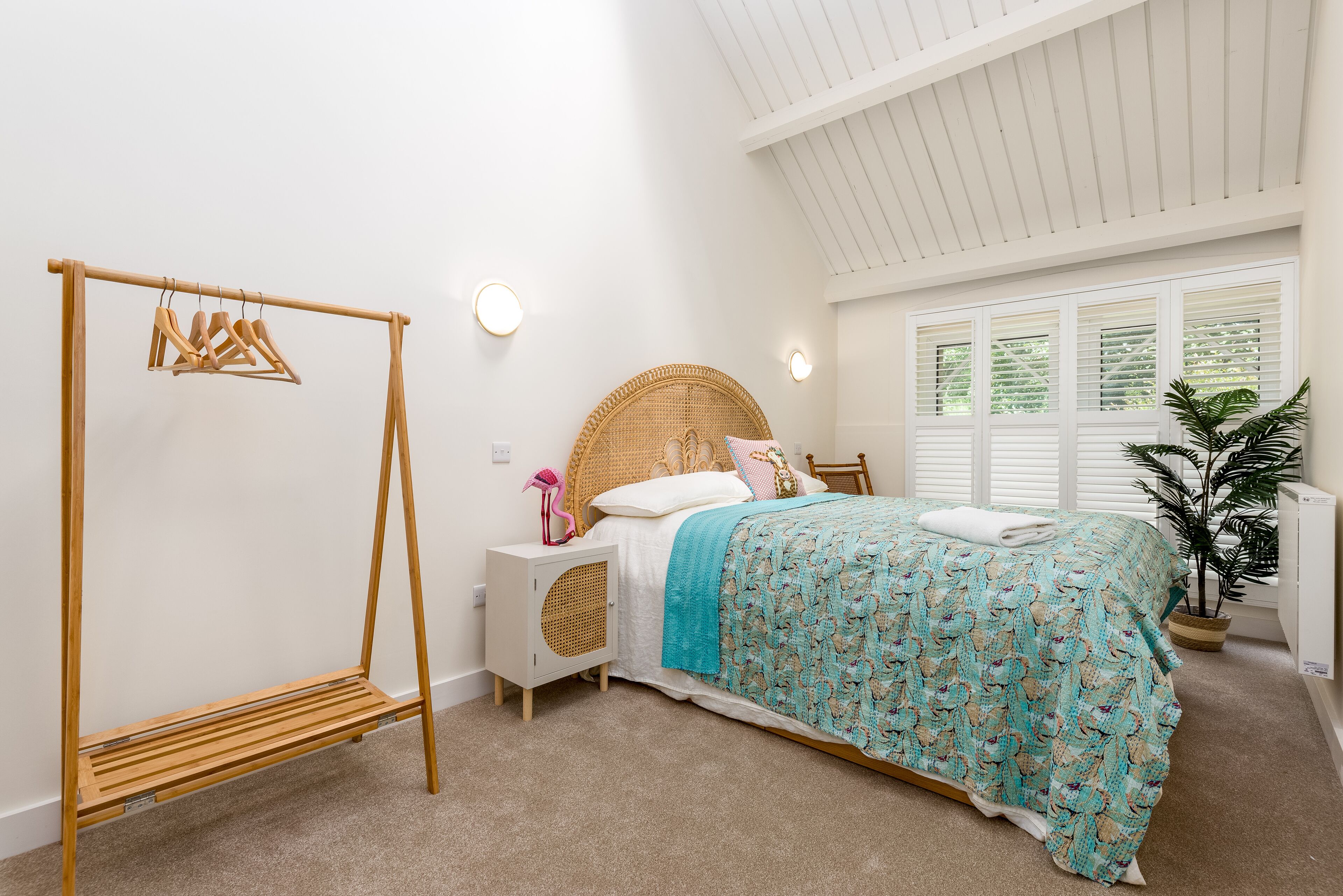 Une chambre à coucher avec un lit, une balançoire en bois, une table de chevet avec une lampe et une fenêtre avec des stores.
