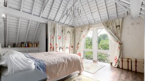 A bedroom with a bed, a desk, a chandelier, curtains, and a view of greenery outside. - Luxury Chilterns Hideaway, Easy Access to London (Reading)