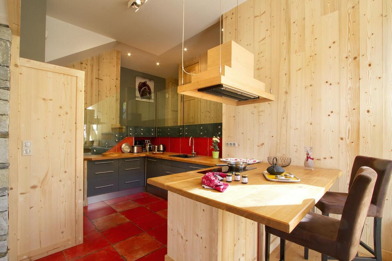 Een moderne keuken met houten wanden, een vloer van rode tegels en een centraal eiland met zitplaatsen.
