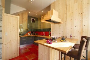 A modern kitchen with wooden walls, a red tiled floor, and a central island with seating. - Chalet, view mountain, terrace, balcony, fireplace or stove, parking, tv, 162m², Les 2 Alpes (Les Deux Alpes)