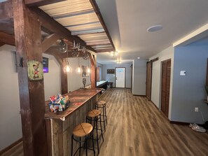 A bar area with wooden stools, pendant lighting, and a snack bar.