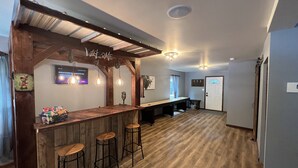 Una zona de bar con taburetes de madera, una barra alargada e iluminación colgante.