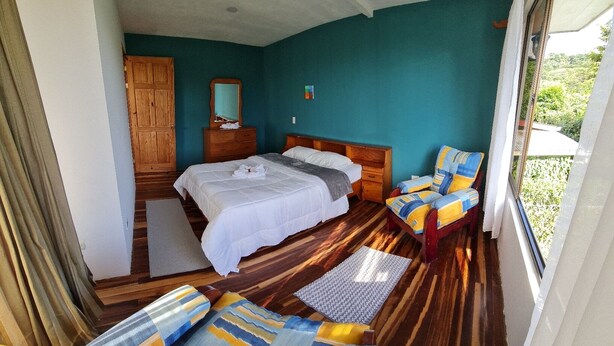 Un dormitorio con cama, una silla, un armario de madera y una ventana.