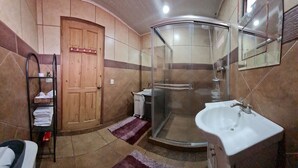 Un baño con cabina de ducha de vidrio, un lavabo, una puerta de madera y una estantería con toallas.