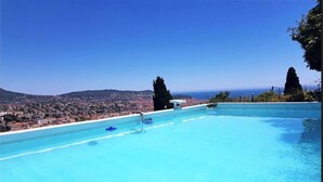 A clear blue infinity pool with a view of a cityscape and the sea in the background.