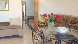A living room with a sofa, a dining table with chairs, a vase with flowers, and a bookshelf.