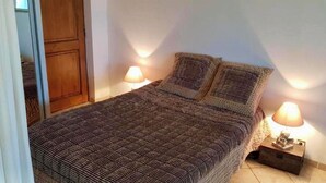 A neatly made bed with a patterned bedspread, two bedside lamps, and a wooden wardrobe in a room with white walls.