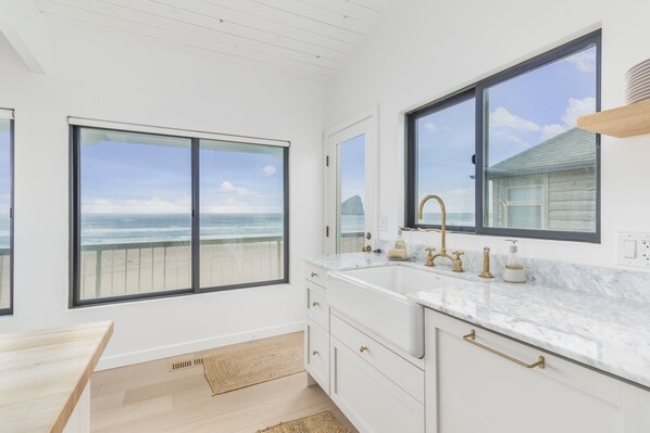 Enjoy a beach view from the bathroom window, featuring a sink with gold fixtures and a minimalist design.