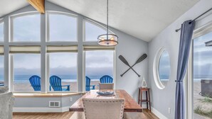 A dining area with a view of the beach, featuring a wooden table, blue chairs, and a large window.