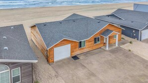 A beachfront property with a wooden house, a garage, and a covered patio area.
