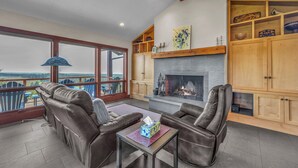 A spacious living area with a fireplace, leather sofas, a coffee table, and a large window offering a scenic view. - Incredible Ocean/Esturary Views, Large Covered Deck, Community Pool and Hot Tub (Pacific City)