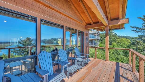 A wooden deck with Adirondack chairs and a view of a lake and mountains. - Incredible Ocean/Esturary Views, Large Covered Deck, Community Pool and Hot Tub (Pacific City)