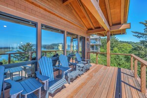 A wooden deck with Adirondack chairs and a view of a lake and mountains. - Incredible Ocean/Esturary Views, Large Covered Deck, Community Pool and Hot Tub (Pacific City)