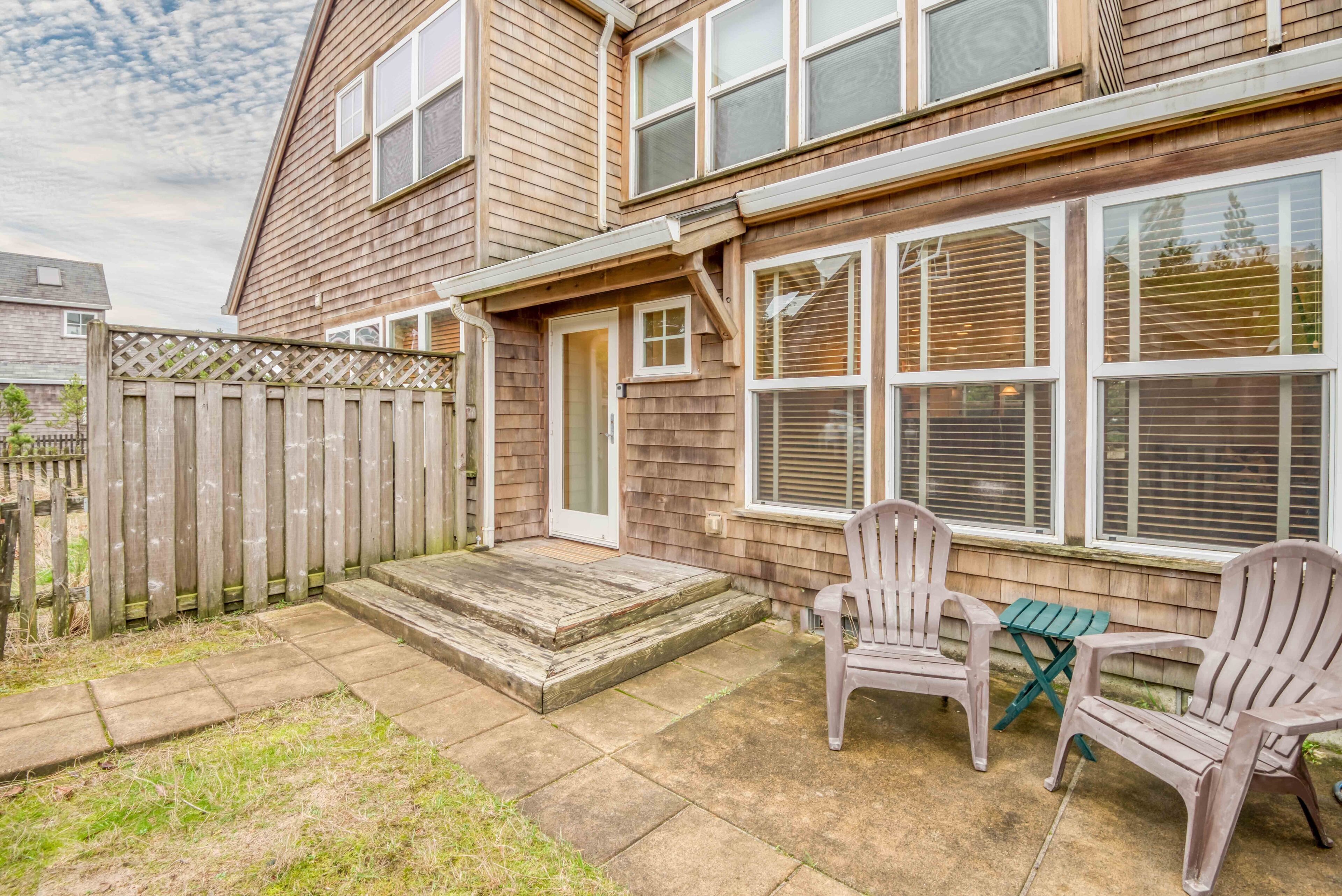 Une maison à deux étages avec un porche à l’avant, une clôture en bois et deux fauteuils Adirondack.