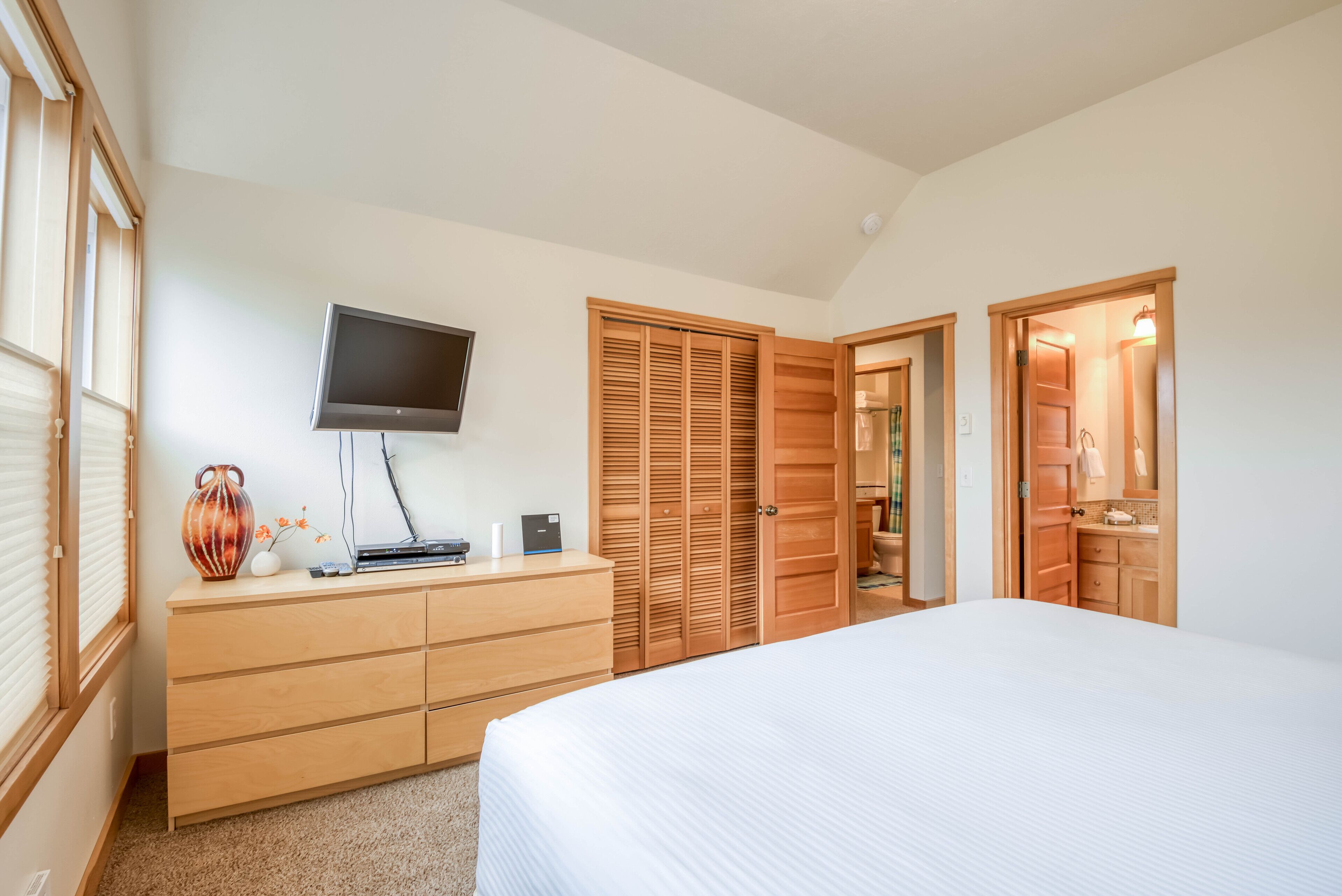 A bedroom with a bed, a dresser, a television, and a wooden closet.