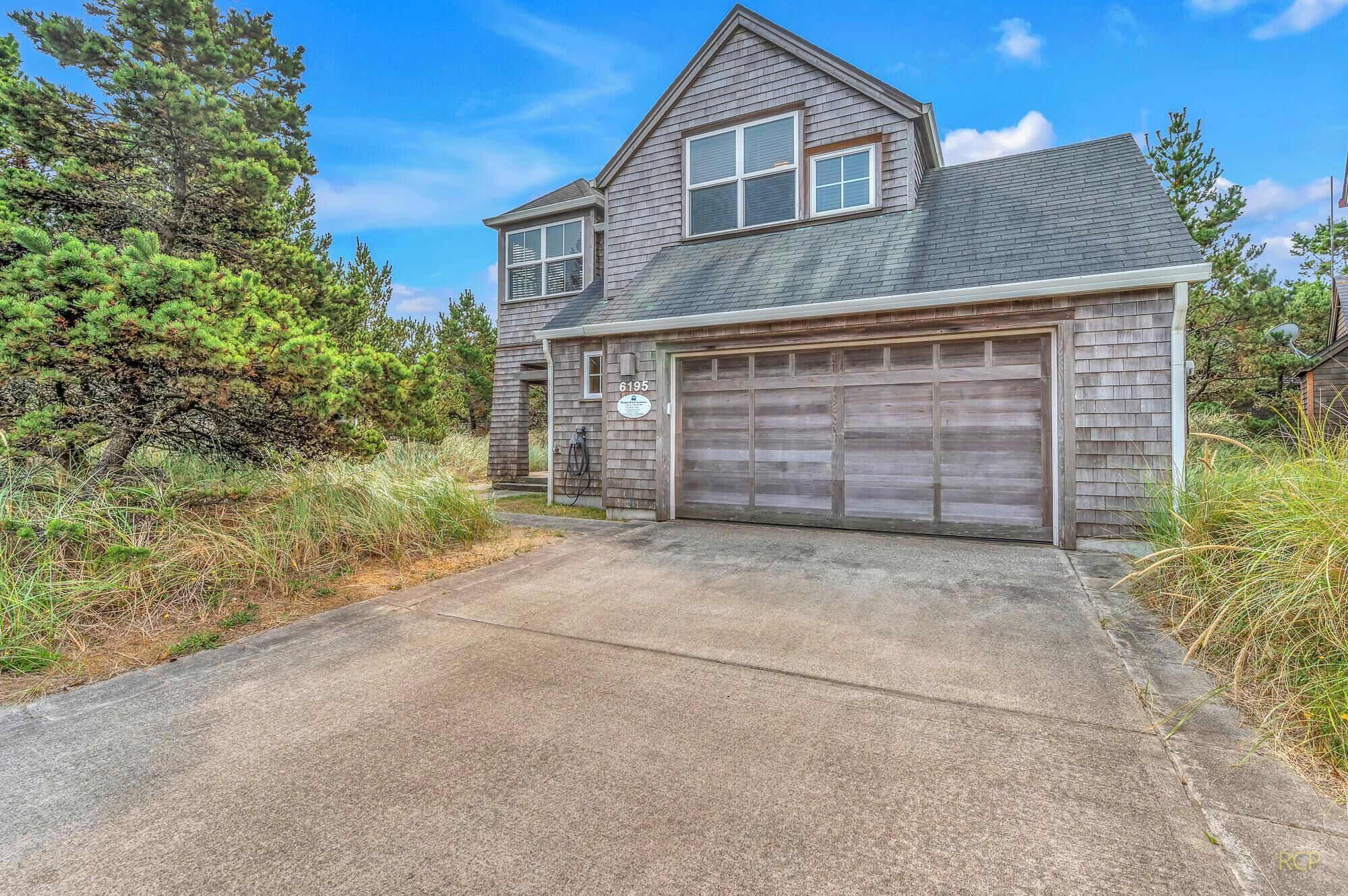 A two-story house with a garage, a driveway, and a large tree in the background.