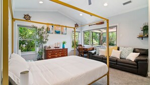 A bedroom with a four-poster bed, a wooden dresser, a desk, and a leather sofa.