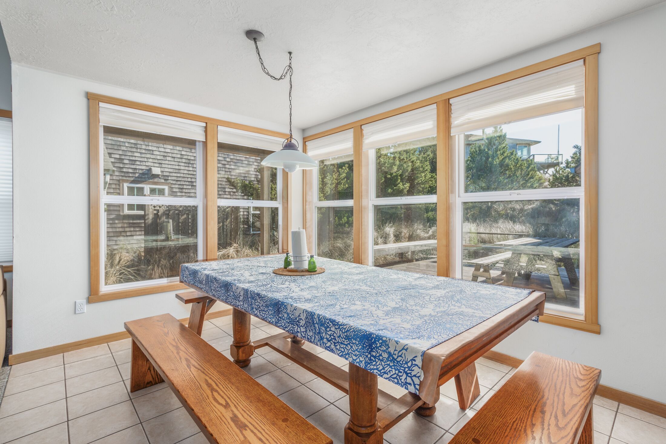 A dining area with a table covered by a blue and white patterned tablecloth, wooden benches, and a hanging light fixture.