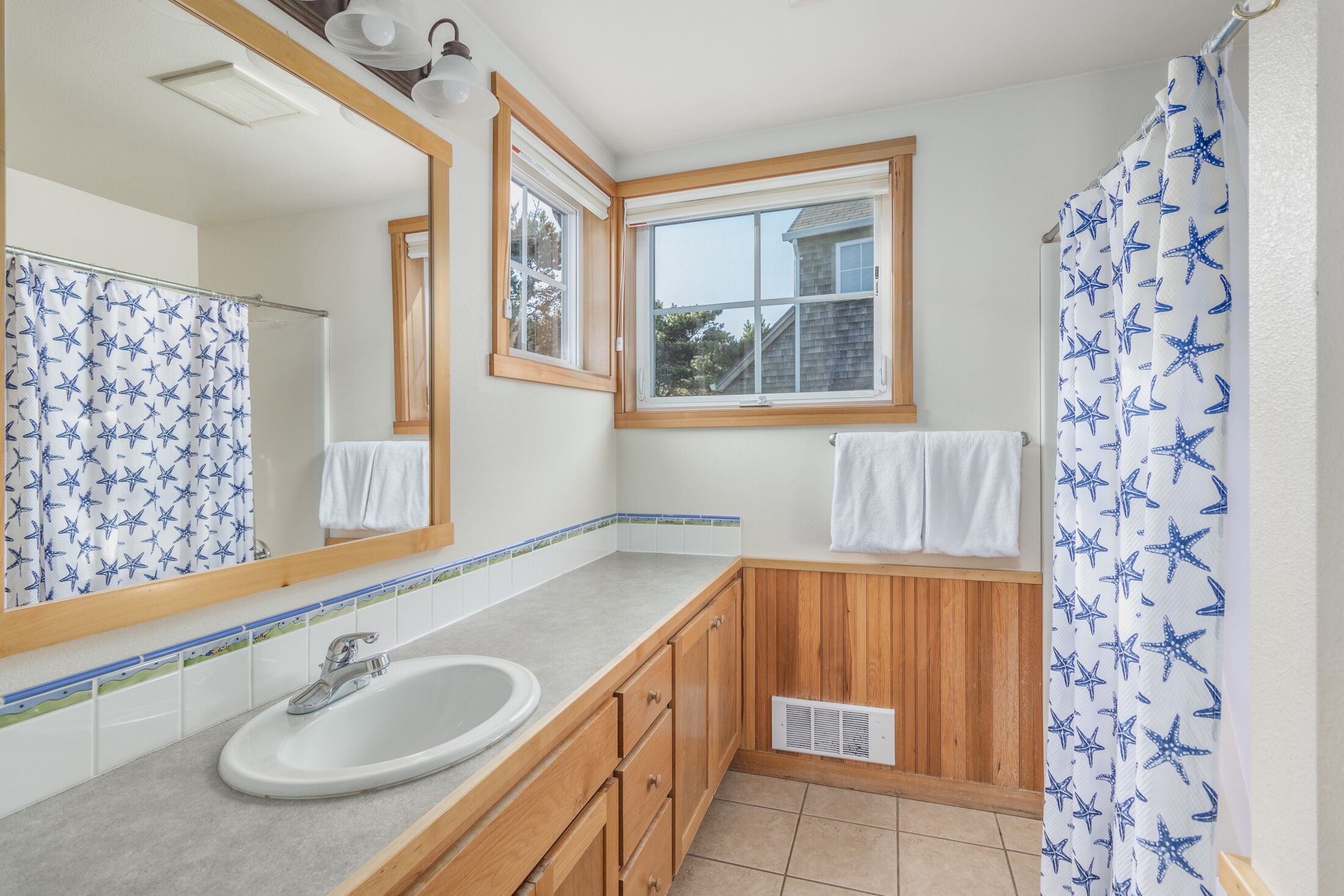 A bathroom with a white sink, wooden cabinets, a window, and a shower curtain with star patterns.