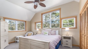 A bedroom with a large bed, two bedside tables, a chair, a wardrobe, and a ceiling fan. - Delightfully Decorated Home Walking Distance to the Beach, Fireplace, Deck, BBQ (Pacific City)