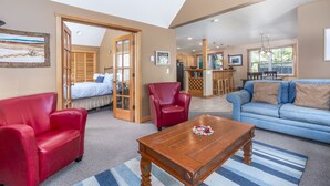 A spacious living area with a large sofa, a red armchair, a wooden coffee table, and a bed with a view. - Delightfully Decorated Home Walking Distance to the Beach, Fireplace, Deck, BBQ (Pacific City)