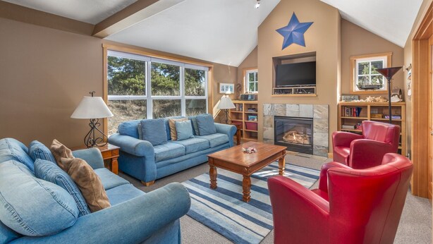 A spacious living room with a high ceiling, a fireplace, a star decoration, and a large window. - Delightfully Decorated Home Walking Distance to the Beach, Fireplace, Deck, BBQ (Pacific City)